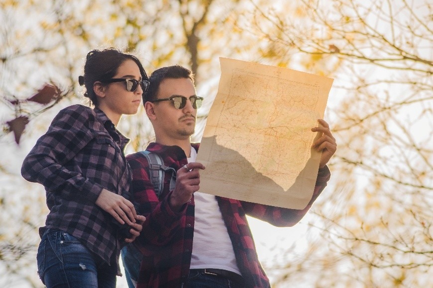 A couple outdoors, examining a vintage map while enjoying a sunny day, suggesting exploration and adventure in nature.